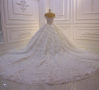 Robe de mariée longue princesse en tulle, décolleté cœur, épaules dénudées, dos nu, ornée d'appliques en dentelle et de volants.