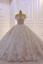 Robe de mariée longue princesse en tulle, décolleté cœur, épaules dénudées, dos nu, ornée d'appliques en dentelle et de volants.