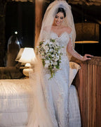 Vestido de novia de tul corte sirena, manga larga, hombros descubiertos, con apliques de encaje y mangas largas.