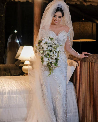 Vestido de novia de tul corte sirena, manga larga, hombros descubiertos, con apliques de encaje y mangas largas.