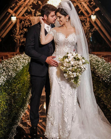 Vestido de novia de tul corte sirena, manga larga, hombros descubiertos, con apliques de encaje y mangas largas.