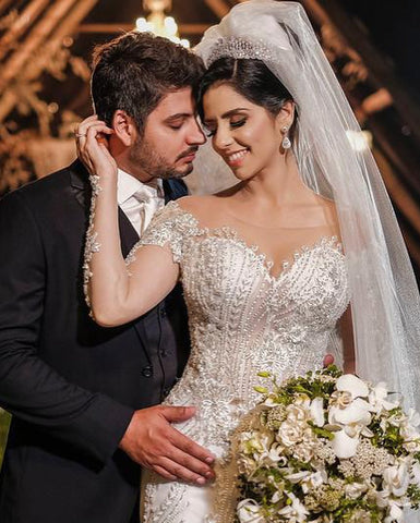 Vestido de novia de tul corte sirena, manga larga, hombros descubiertos, con apliques de encaje y mangas largas.