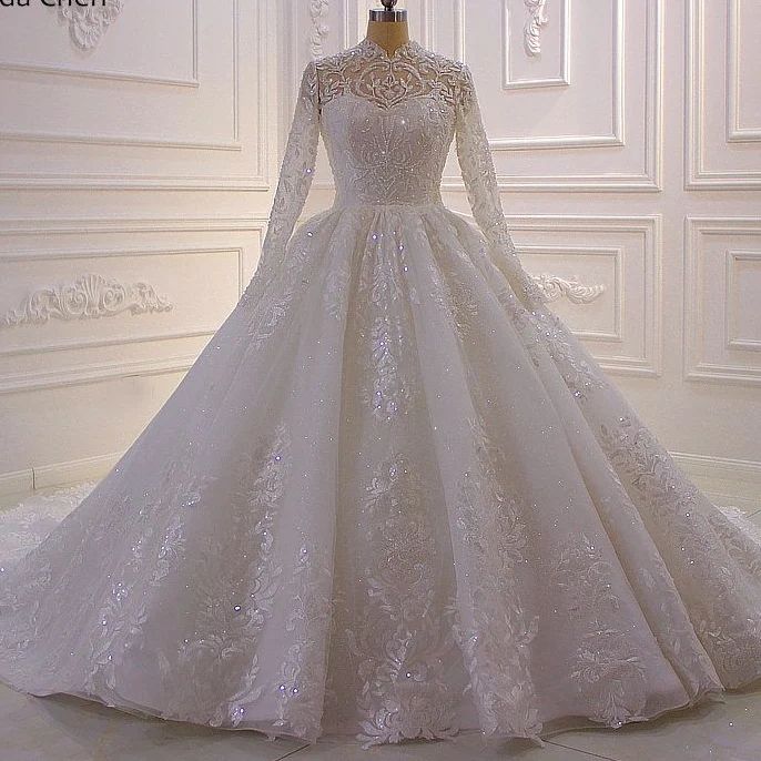 Lujoso vestido de novia de encaje con lentejuelas, corte línea A y cuello alto, con mangas largas.