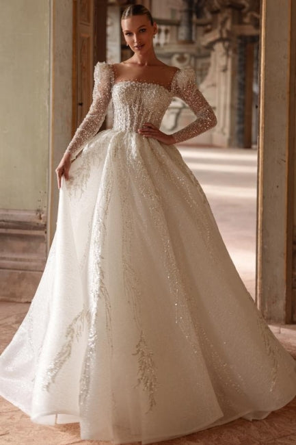 Robe de mariée longue ivoire luxueuse, coupe trapèze, col carré, ornée de dentelle et de perles, manches longues