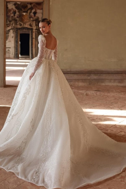 Robe de mariée longue ivoire luxueuse, coupe trapèze, col carré, ornée de dentelle et de perles, manches longues