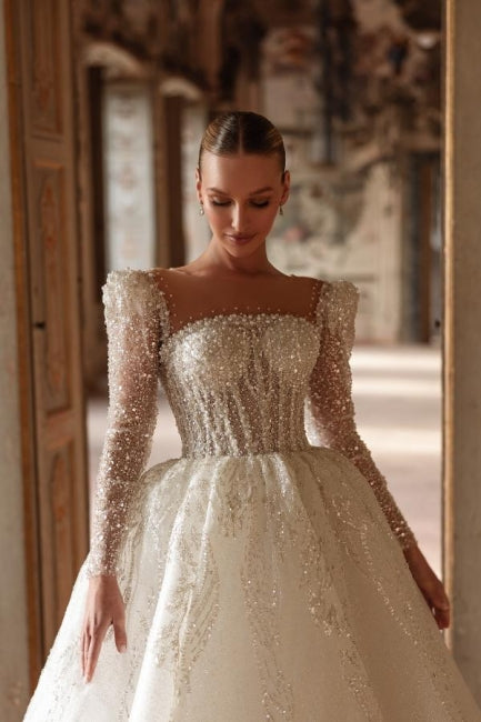 Robe de mariée longue ivoire luxueuse, coupe trapèze, col carré, ornée de dentelle et de perles, manches longues