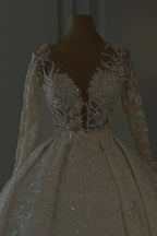 Vestido de novia largo de encaje color marfil, corte en A, escote en V, mangas largas y brillo, con lentejuelas.