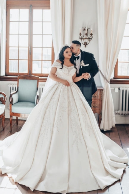 Luxueuse robe de mariée longue blanche en satin, coupe trapèze, épaules dénudées et dentelle.