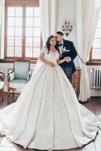 Luxueuse robe de mariée longue blanche en satin, coupe trapèze, épaules dénudées et dentelle.