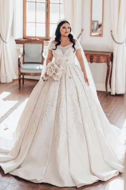Luxueuse robe de mariée longue blanche en satin, coupe trapèze, épaules dénudées et dentelle.