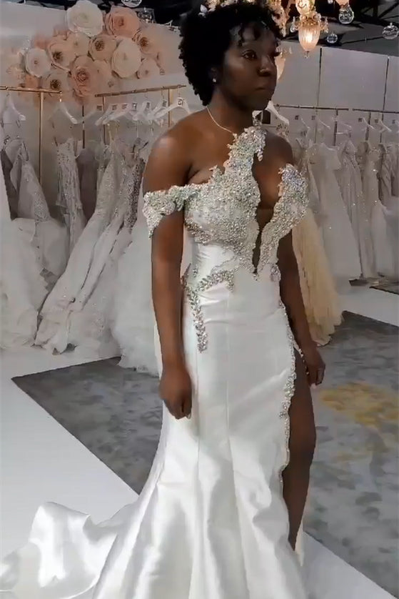 Robe de mariée blanche longue et luxueuse, asymétrique, sans manches, ornée de bijoux et avec traîne amovible.