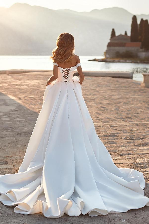 Robe de mariée sobre en satin froncé, longue, trapèze, épaules dénudées, ornée de cristaux