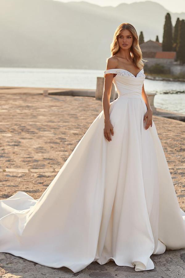 Robe de mariée sobre en satin froncé, longue, trapèze, épaules dénudées, ornée de cristaux