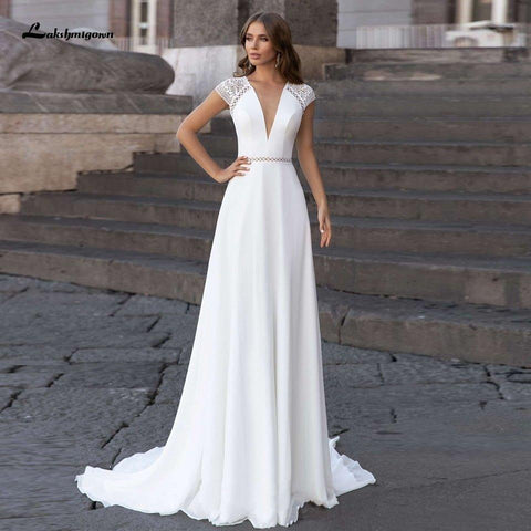 Vestido de novia Abiti Donna Modest Bridal corte A, verano 2025. Sencillo, con escote en V, espalda descubierta, ideal para bodas en la playa. Cola larga.
