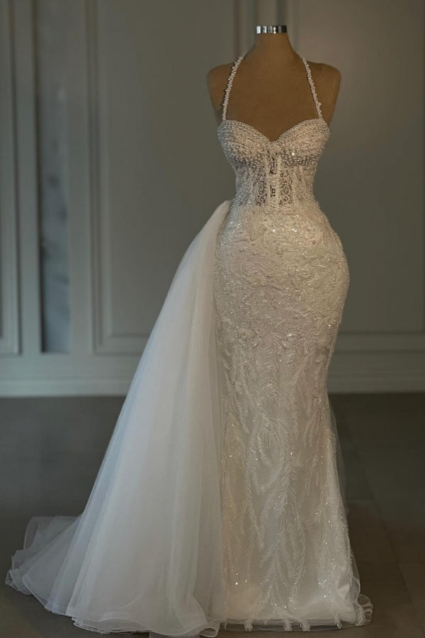 Vestido de novia largo de sirena color marfil con cuello halter, encaje, cuentas y sin mangas.