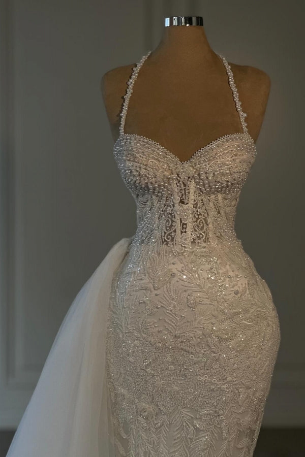 Vestido de novia largo de sirena color marfil con cuello halter, encaje, cuentas y sin mangas.
