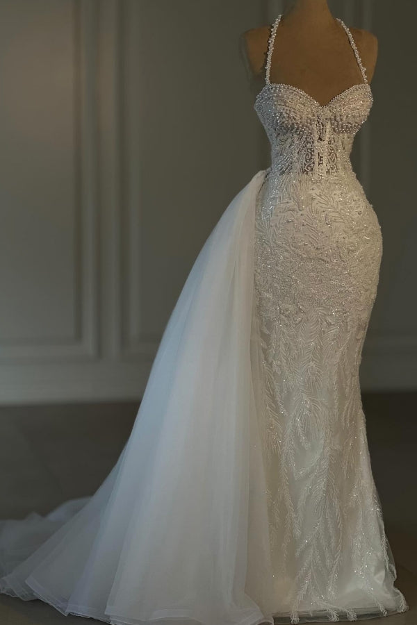 Vestido de novia largo de sirena color marfil con cuello halter, encaje, cuentas y sin mangas.