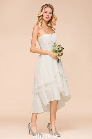 Vestido de dama de honor romántico blanco/marfil con escote corazón y corte asimétrico, sin mangas, ideal para bodas en la playa.