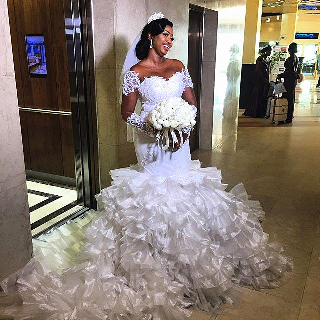Vestido de novia de sirena con hombros descubiertos, manga corta y cola con volantes.