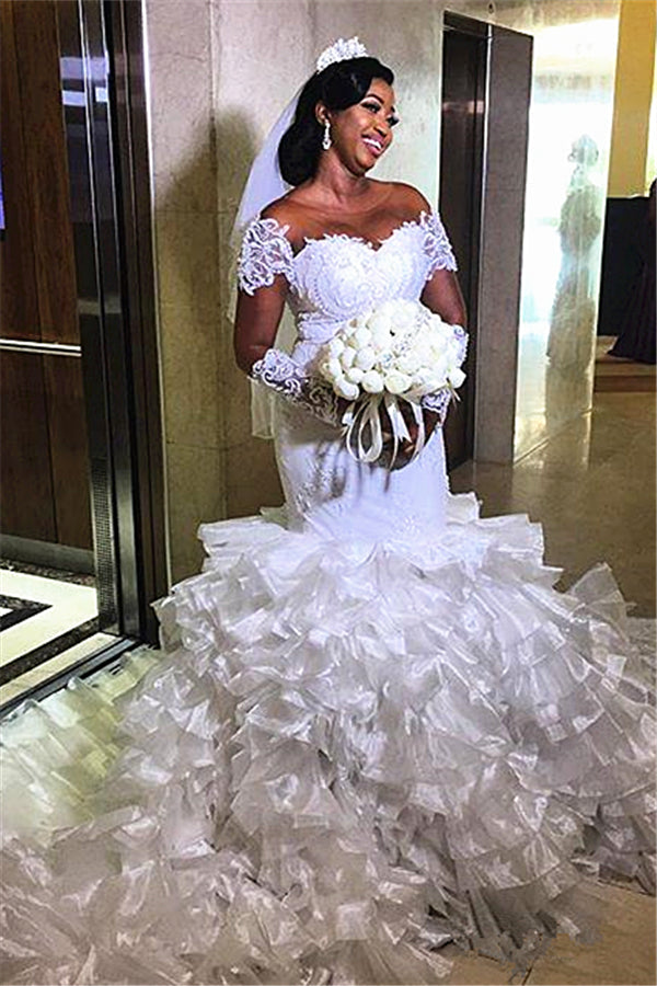 Vestido de novia de sirena con hombros descubiertos, manga corta y cola con volantes.