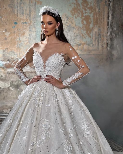 Robe de mariée tendance en dentelle, coupe trapèze, col en V, manches longues et appliques, longueur au sol.