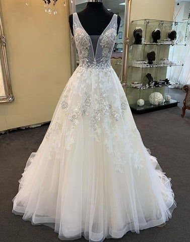 Robe de mariée unique longue en tulle et dentelle perlée, col en V, coupe trapèze.