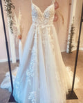 Robe de mariée vintage longue trapèze à fines bretelles, ornée d'appliqués de dentelle et d'une traîne.